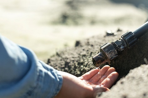 Mans hand catches water coming from drip irrigation pipe