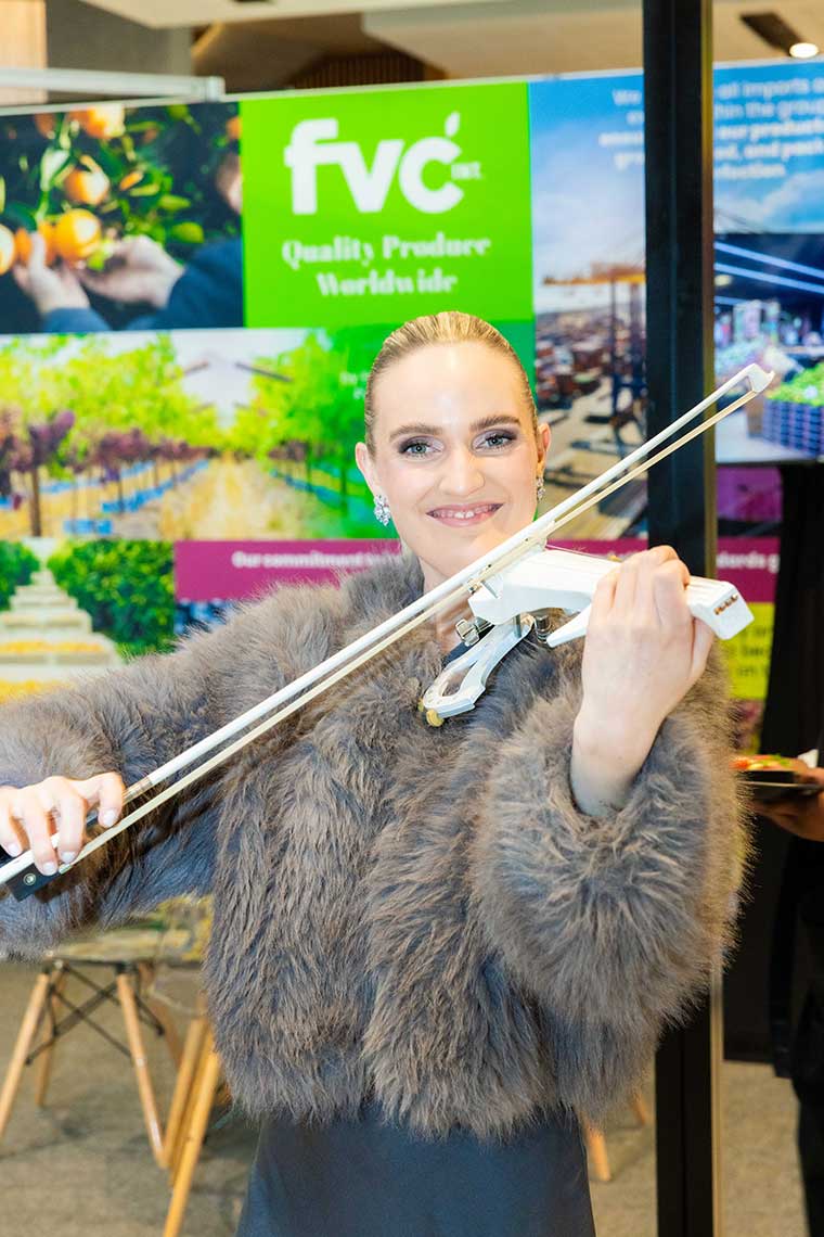 Person playing a white electric violin in front of a vibrant promotional display.