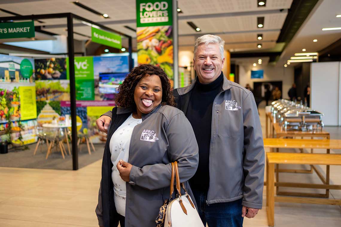 Two smiling individuals wearing "APAC 15" jackets at a conference.