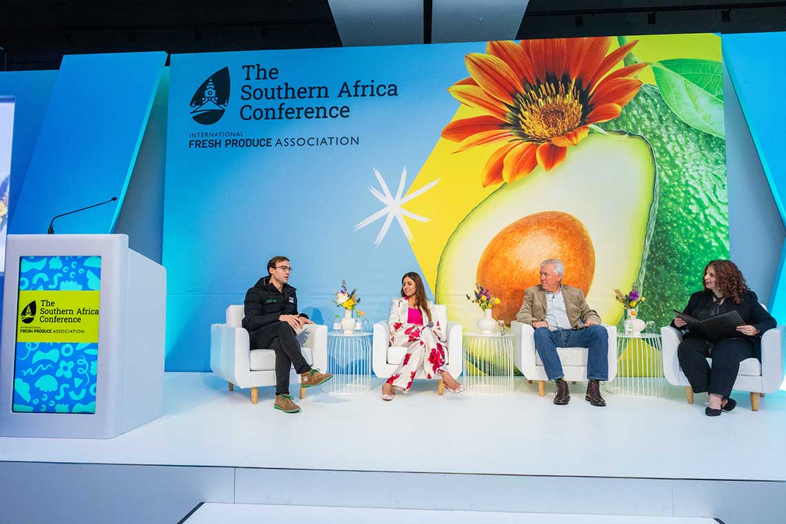 Panel discussion at the Southern Africa Conference with four speakers seated on stage in front of a vibrant backdrop featuring an avocado and a flower.