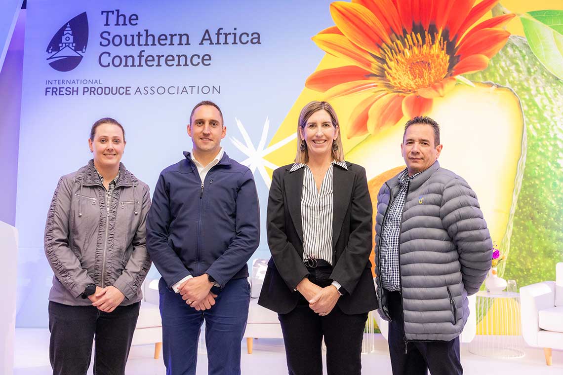 Four people standing in front of a Southern Africa Conference backdrop with a colorful flower design.