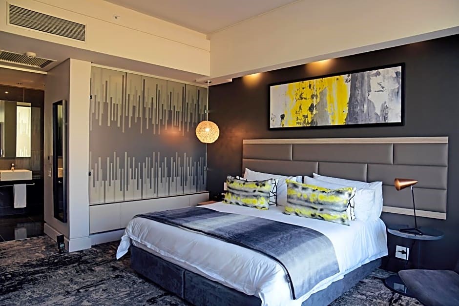 A modern hotel room with a large bed, abstract artwork, and a stylish lamp.