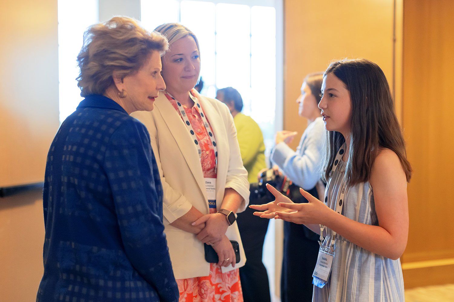 Three women engaged in conversation at an indoor event.