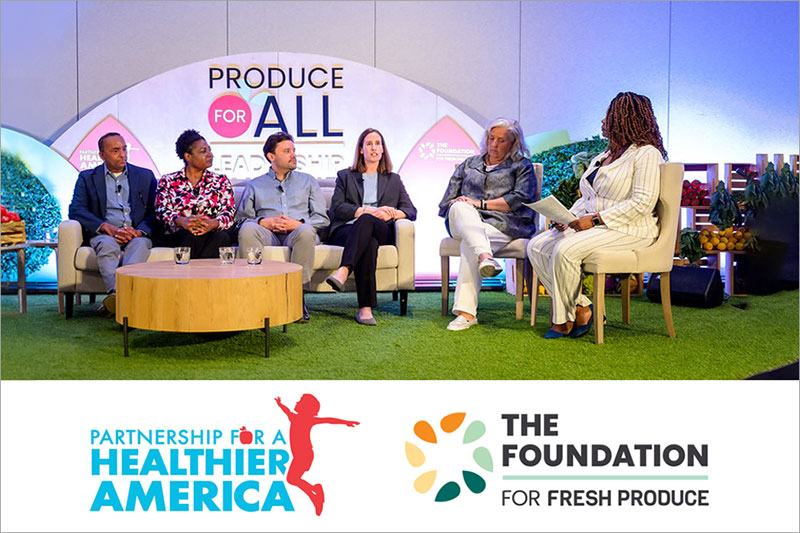 A panel discussion on stage with five people in front of a backdrop reading "PRODUCE FOR ALL," surrounded by greenery and produce.